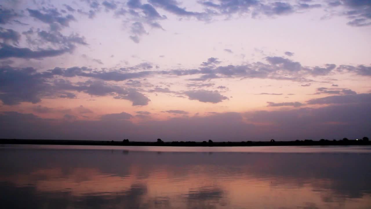 美丽的水景。淡紫色的云漂浮在河上。深红色的云笼罩着湖面。蓝蓝的天空里的彩云倒映在水面上，背景是森林和地平线视频素材