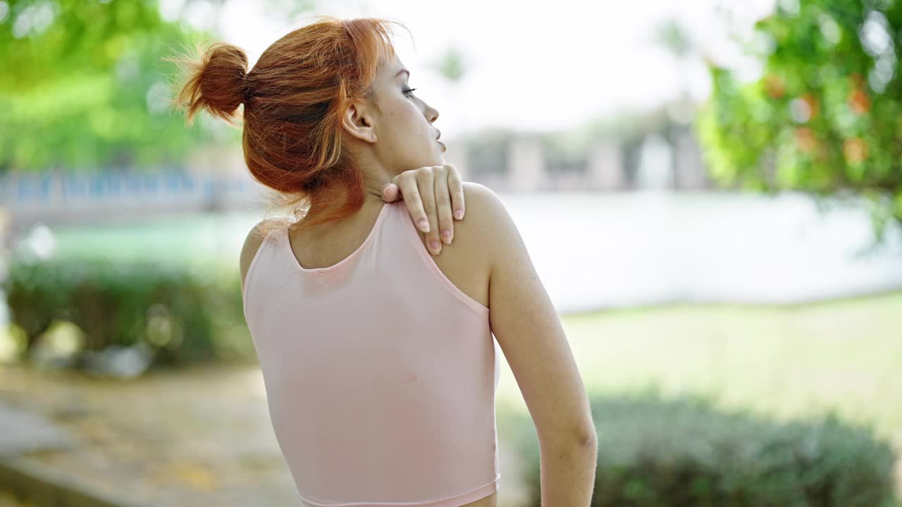 年轻的红发女人穿着运动服在公园里碰着肩膀视频素材