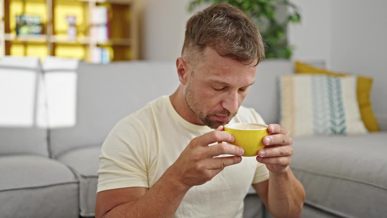 一个年轻人坐在家里的地板上喝咖啡视频素材