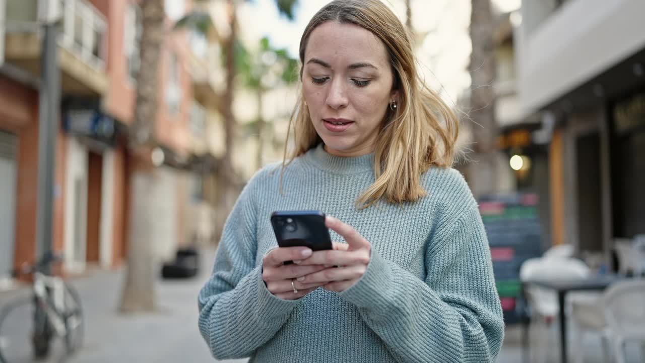 年轻的金发女子在街上用着智能手机，表情严肃视频素材