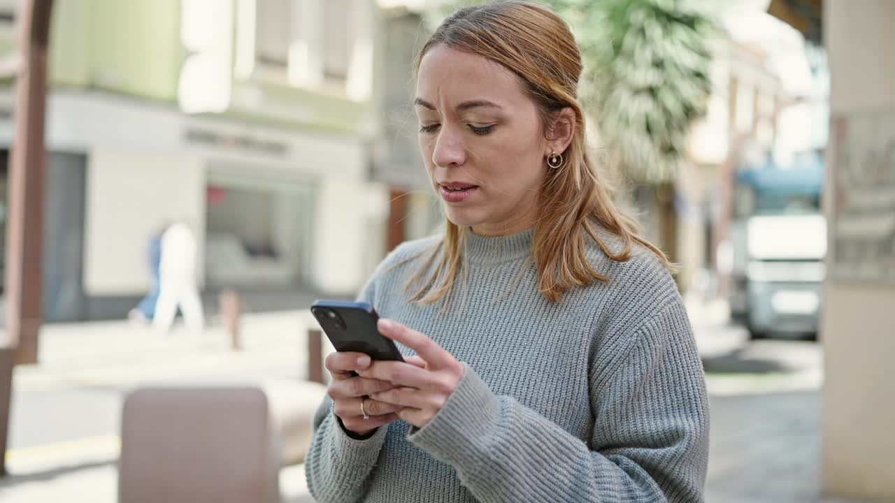 年轻的金发女子在街上用着智能手机，表情严肃视频素材