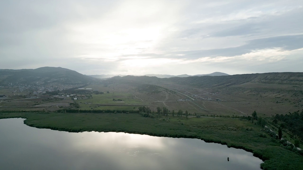 落日灰天映衬着河流，呈现出棕山绿地的景观景象视频素材