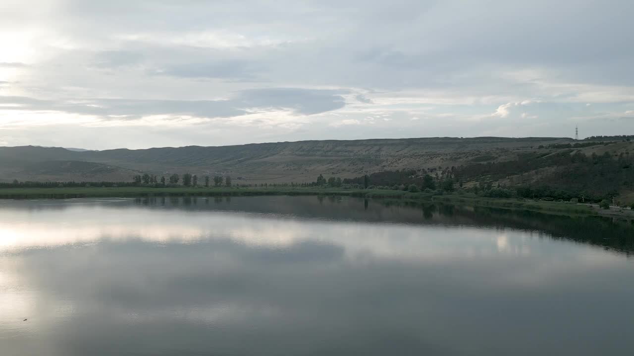 落日灰天映衬着河流，呈现出棕山绿地的景观景象视频素材