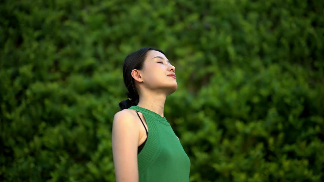 年轻的亚洲女商人站在被绿色植物包围的城市办公园区里沉思。生态户外。可持续的生活方式理念。视频下载