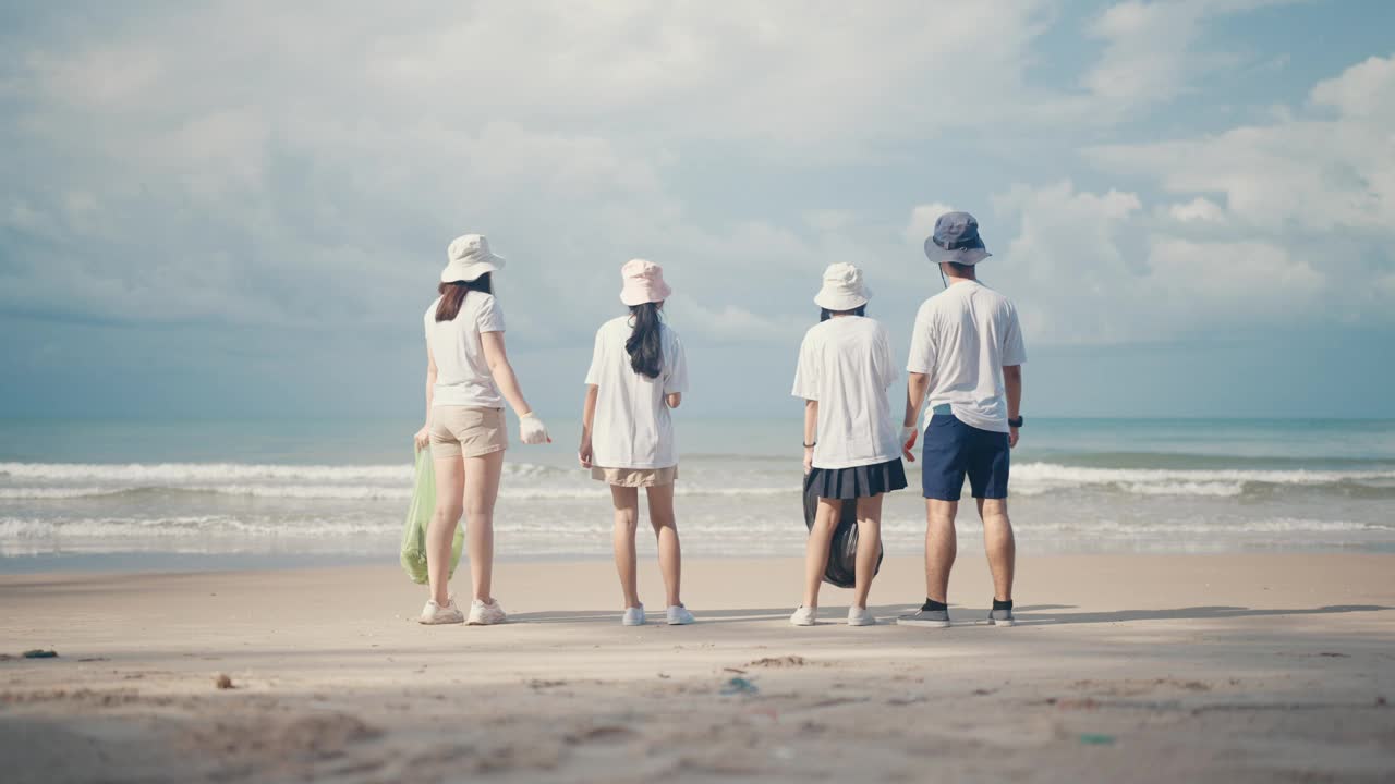 一群亚洲年轻人和孩子在海滩上捡垃圾。愉快地举手，愉快地讲话。视频素材