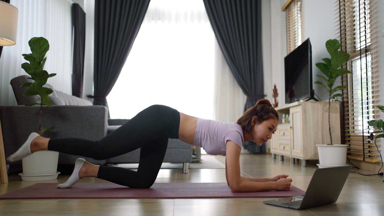 年轻的肌肉健身女性在家里客厅地板上的瑜伽垫上做运动和瑜伽视频素材