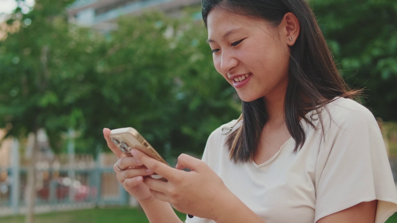 快乐的年轻女子坐在城市公园的长椅上，使用手机视频素材