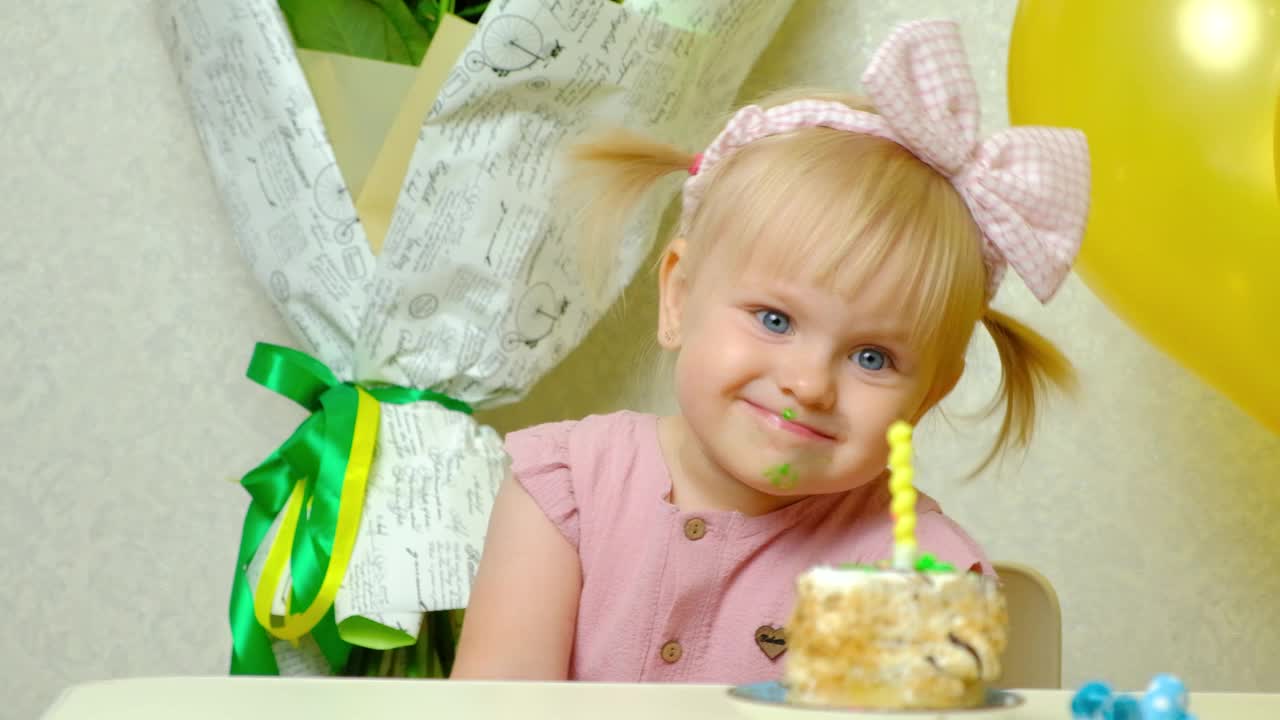 可爱的金发女孩，头上戴着蝴蝶结，吃着生日蛋糕。视频素材