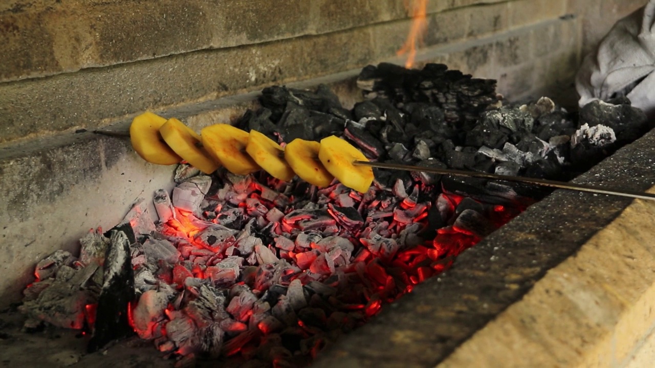 切成大块的土豆串在木炭烤架上烤熟。视频素材