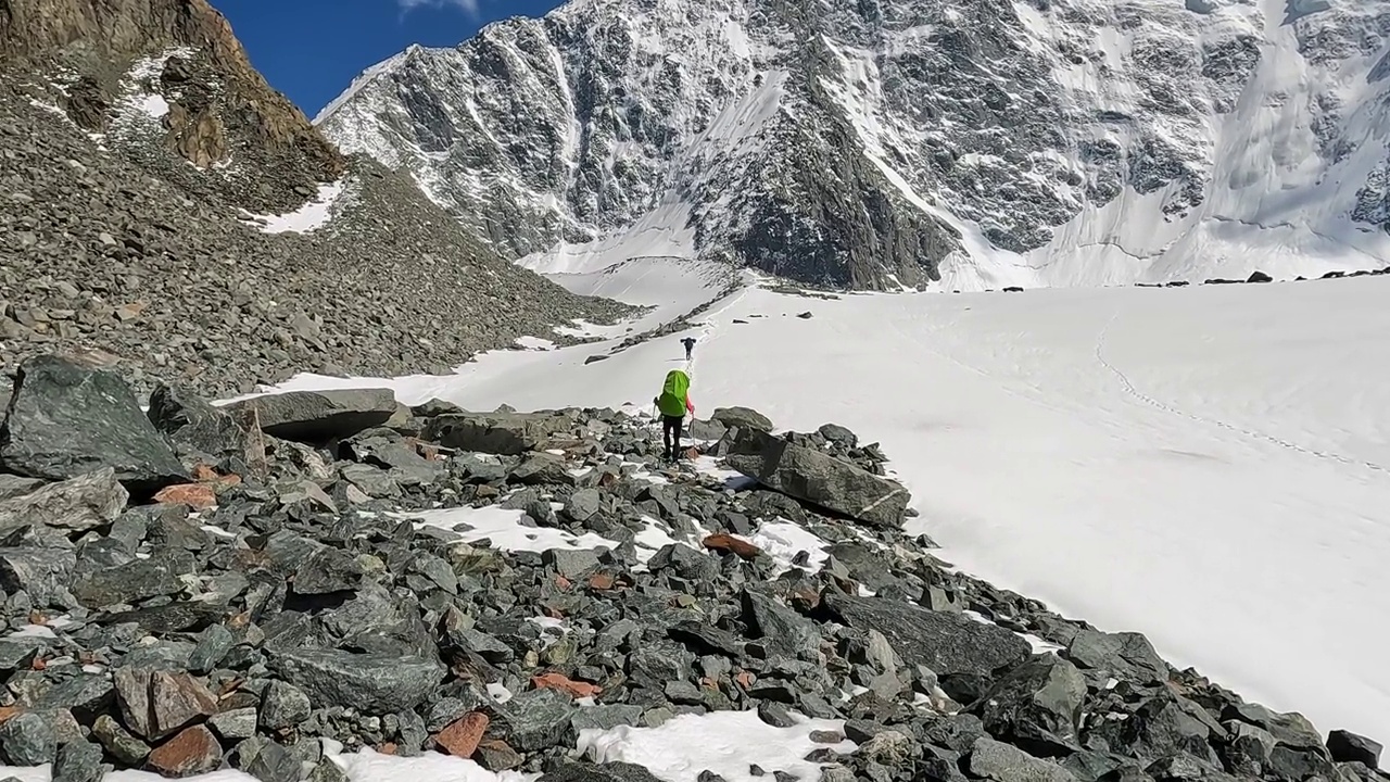 两名背着大背包的登山者走在布满岩石和巨石的雪坡上。视频素材