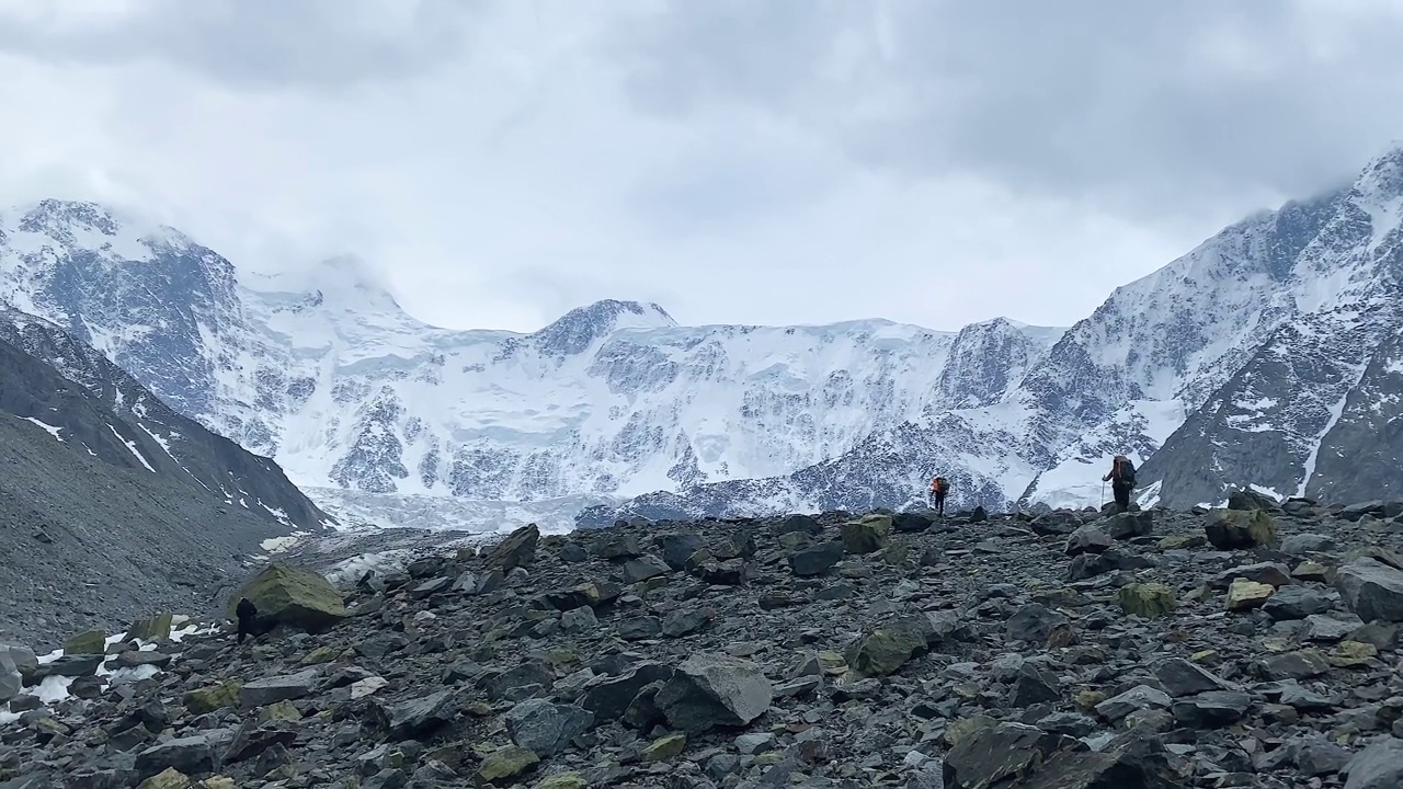 两个背着大背包的登山者正在岩石上行走。Belukha攀升。令人惊叹的阿克姆长城，阿尔泰，俄罗斯视频素材