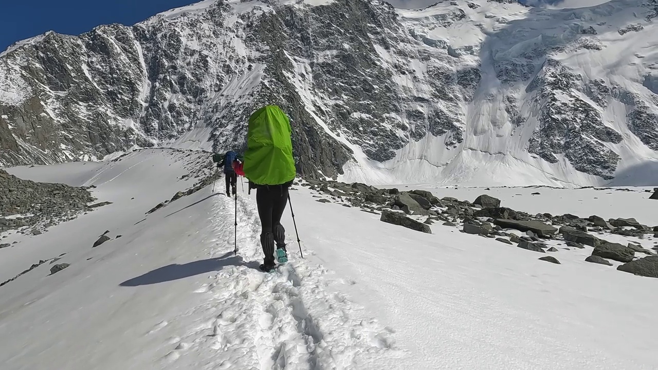 两个背着大背包的登山者正沿着雪道走在山上。视频素材