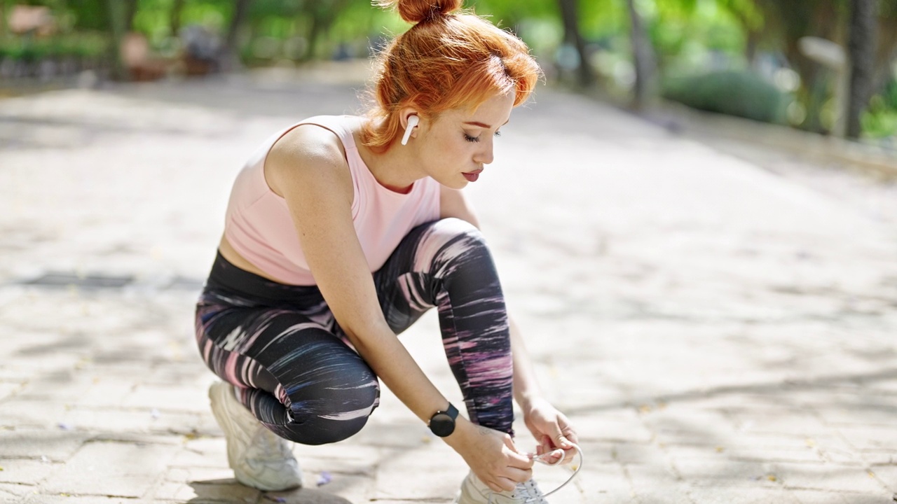 穿着运动服的年轻红发女子在公园系鞋带视频素材