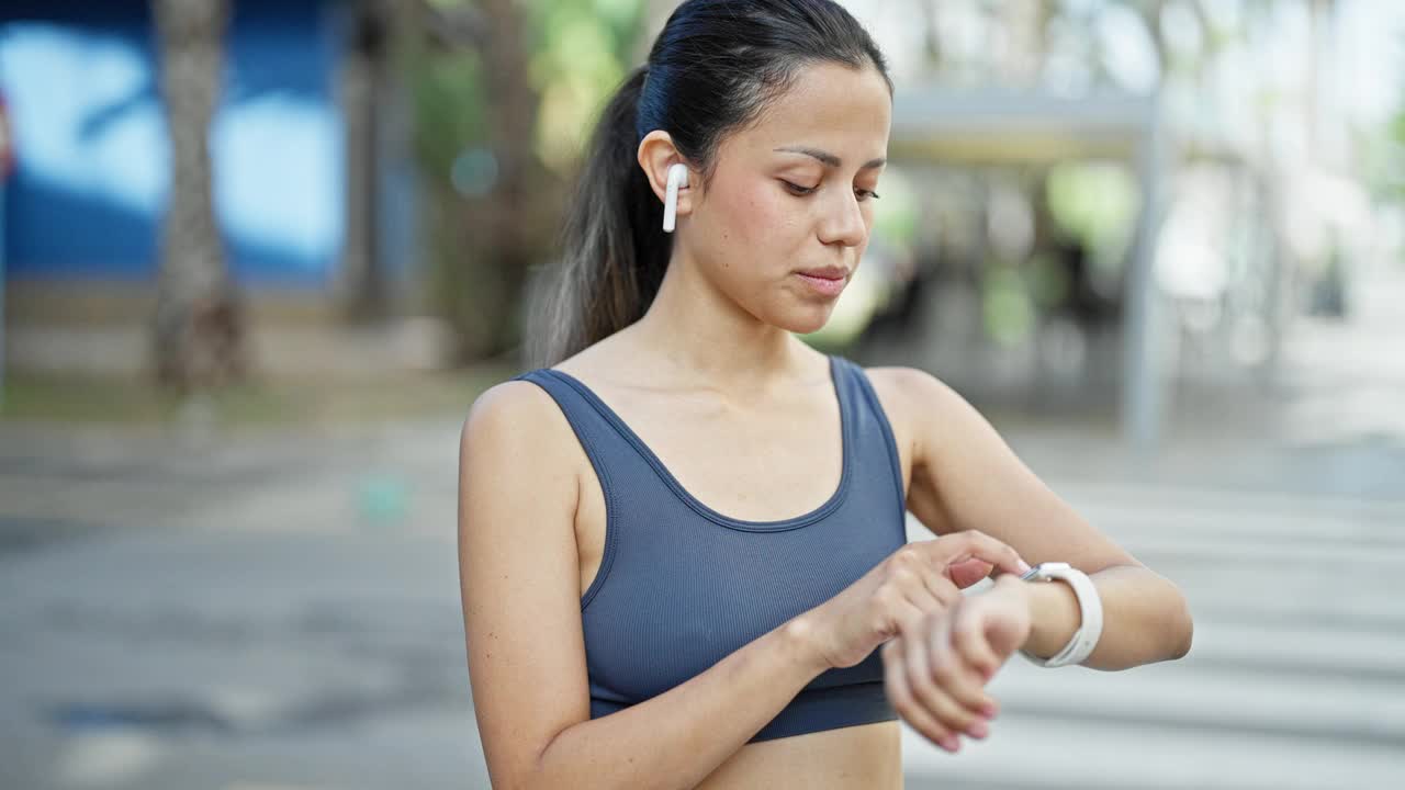 年轻美丽的西班牙妇女穿着运动服，看着秒表在街上视频素材