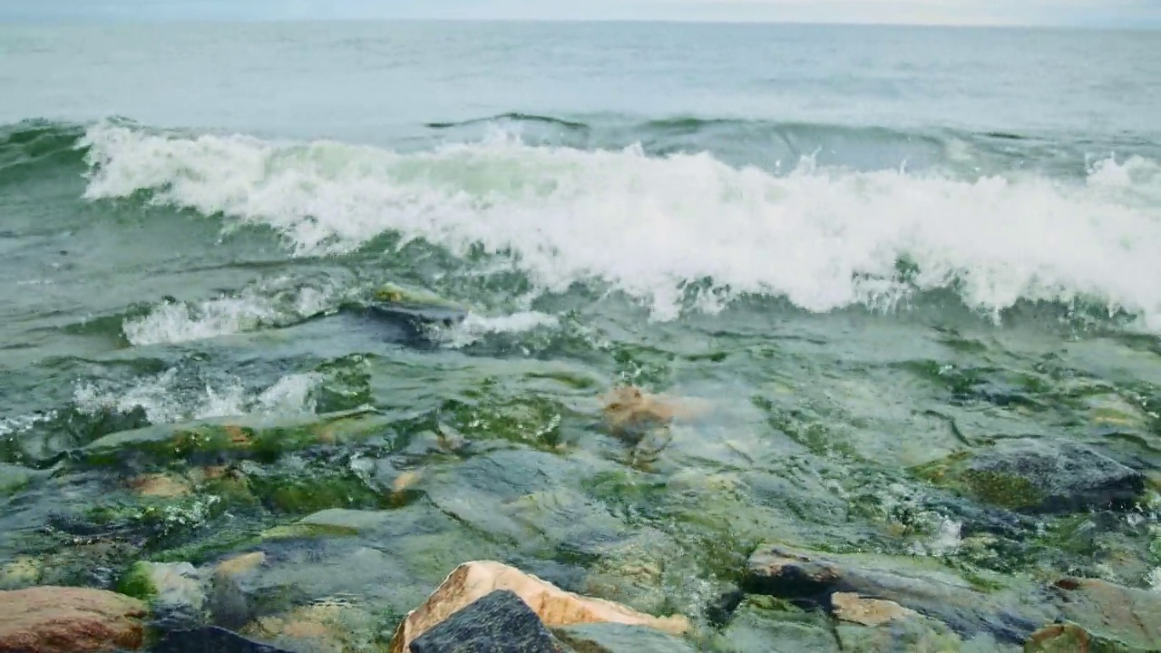 贝加尔湖清澈透明的湖水。海浪拍打着海岸沙滩上的石头。强大的海浪拍打着贝加尔湖的岩石海岸。波浪和水花的特写。美丽的自然景观。视频素材