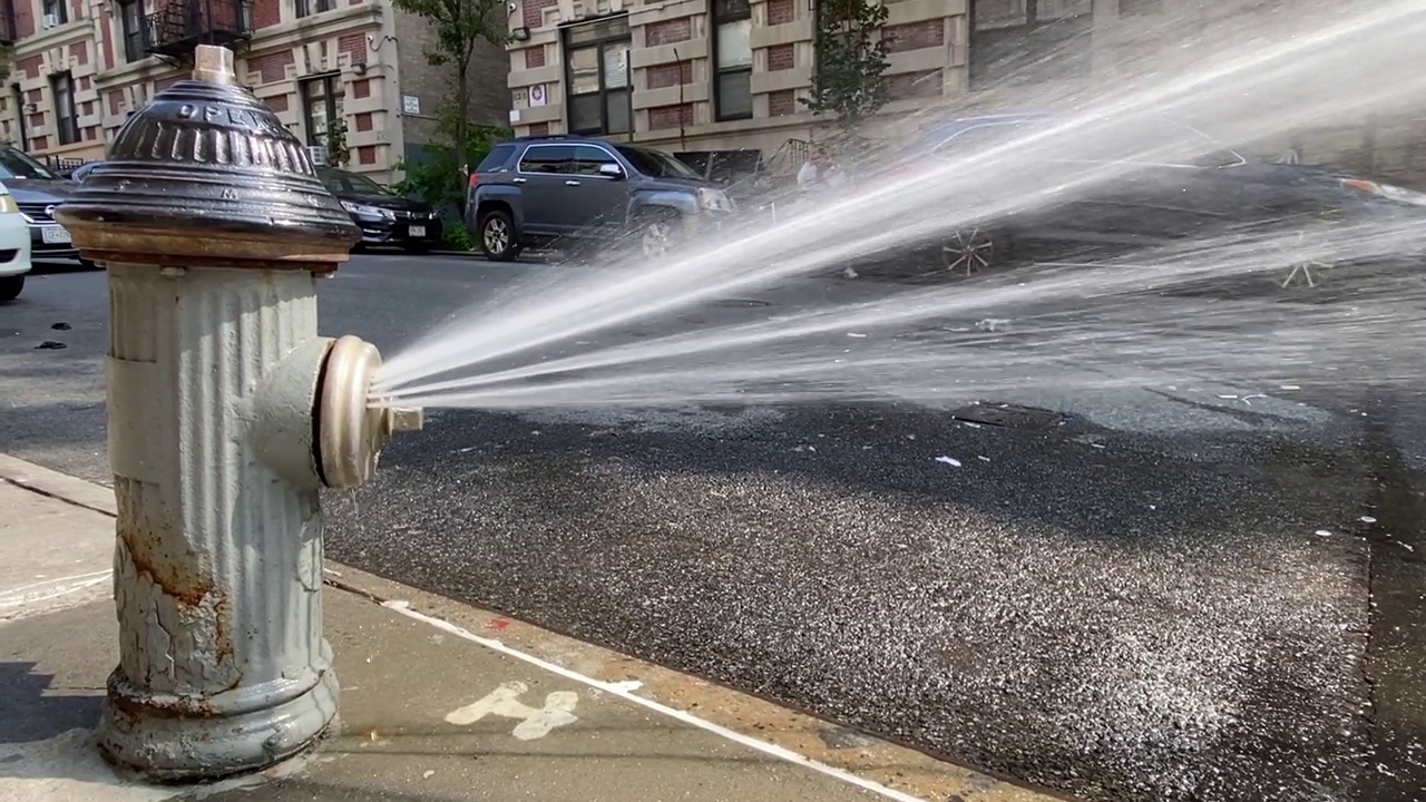 在纽约炎热的夏日，带喷头的消防栓向街道洒水视频下载