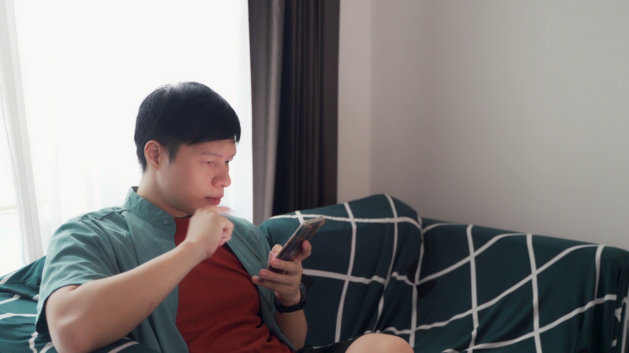 近距离男子在家里躺在沙发上使用智能手机与移动应用程序。男生用手机，上网浏览社交网络。视角相机拍摄。视频下载