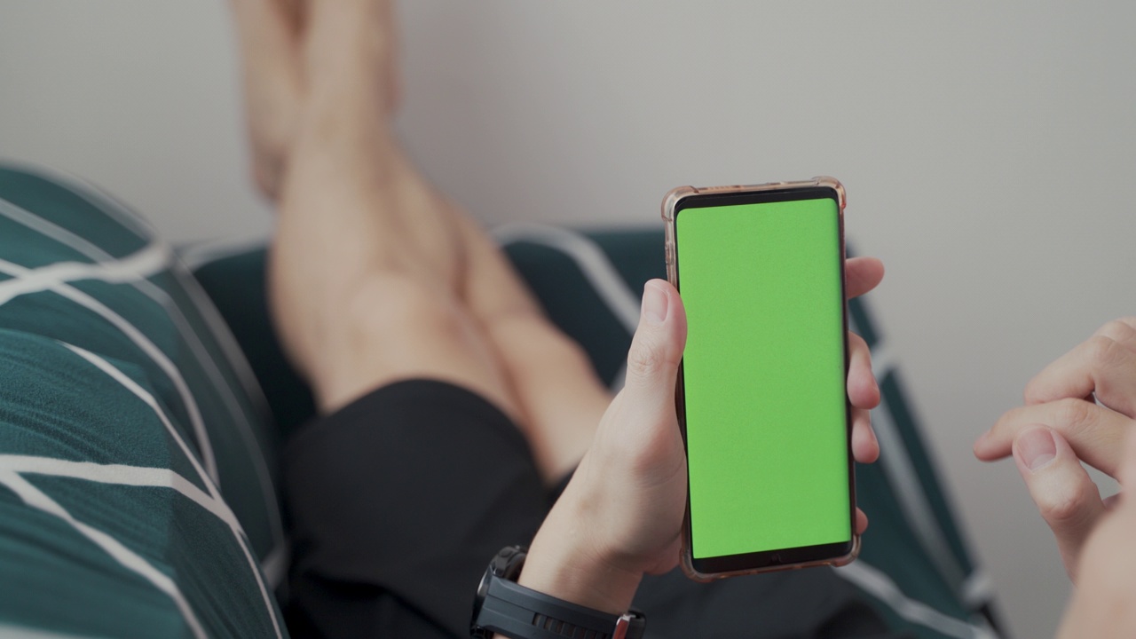 居家男子躺在沙发上使用绿屏智能手机。男生用手机，上网浏览社交网络。视角相机拍摄。视频下载