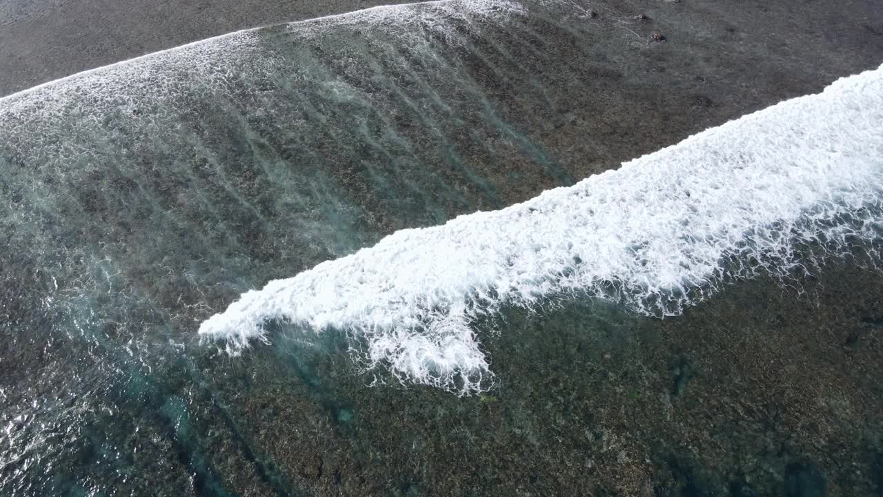 无人机拍摄的海浪到达Nusa Lembongan Jungut Batu村的海岸，海滩上有游船和海藻农场。旅游目的地靠近巴厘岛，印度尼西亚视频素材