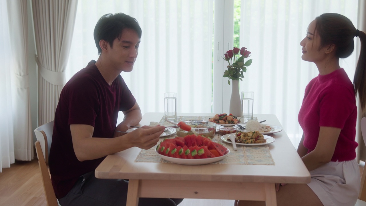 年轻的亚洲夫妇在家里的桌子上吃着食物，轮流喂对方。视频素材