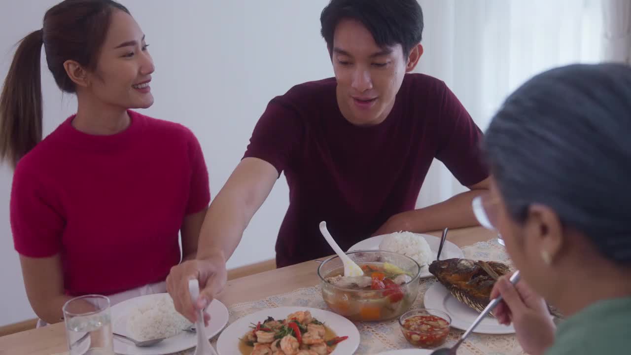 由母亲组成的亚洲家庭。儿子和儿媳正在家里吃饭，把食物放在桌子上。视频素材