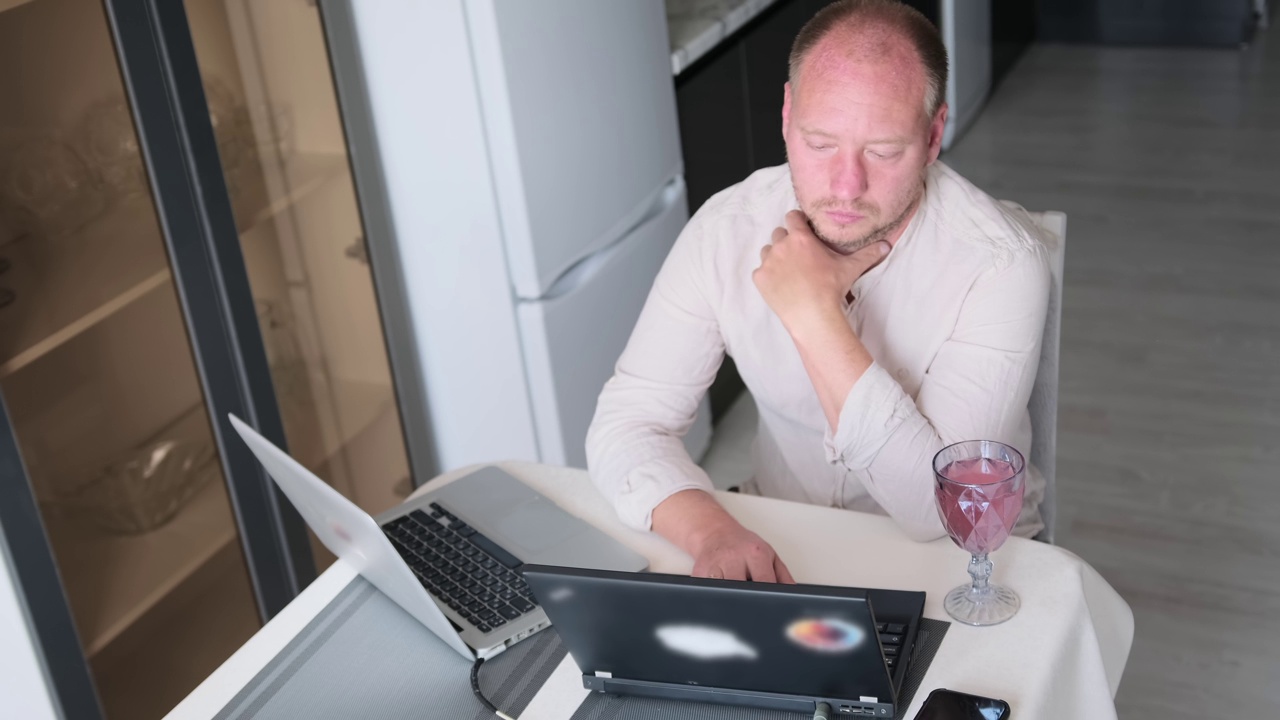 穿着浅色衬衫的白人男子在家工作。IT专家在两台笔记本电脑上用键盘输入程序代码视频素材