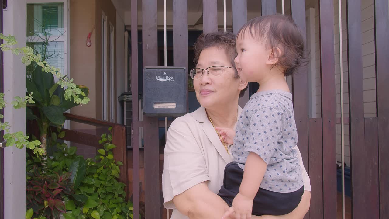 一个亚洲祖父母的家庭，祖母抱着他们年幼的婴儿，蹒跚学步的孩子，孙女，在早上享受着屋外的自然风光视频素材