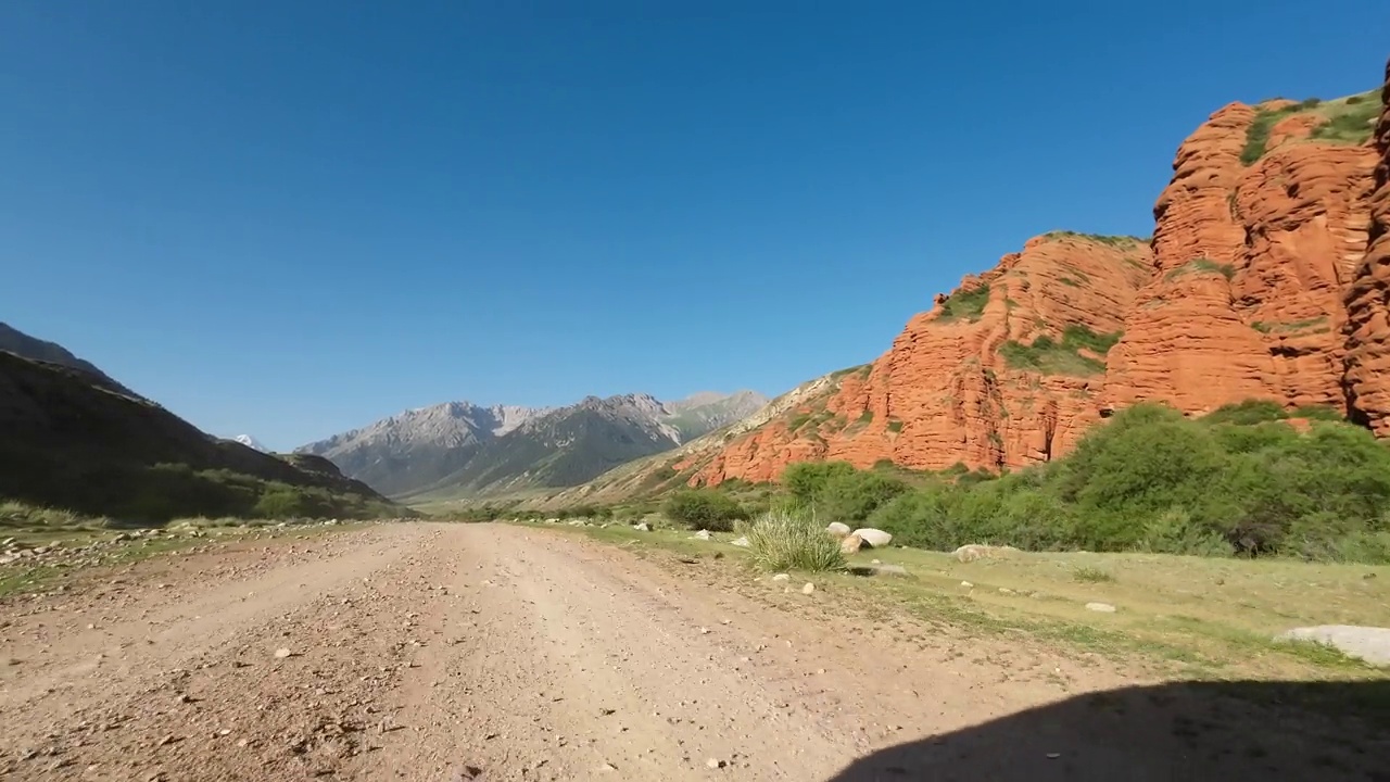 驾车穿过美丽的山峡，一边是红色的岩石，前面是山峰。汽车的观点视频素材