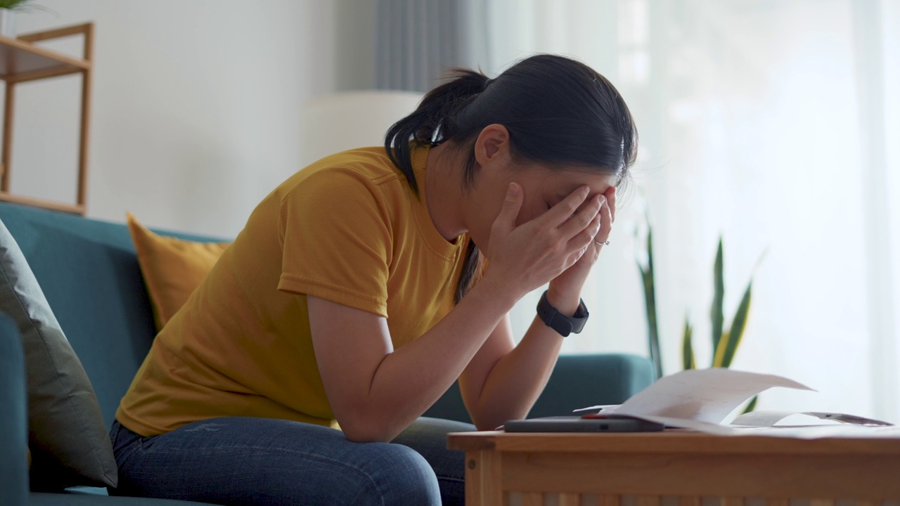 亚洲女性坐在沙发上，担心银行票据、抵押贷款债务和生活成本的账单支付问题。视频素材