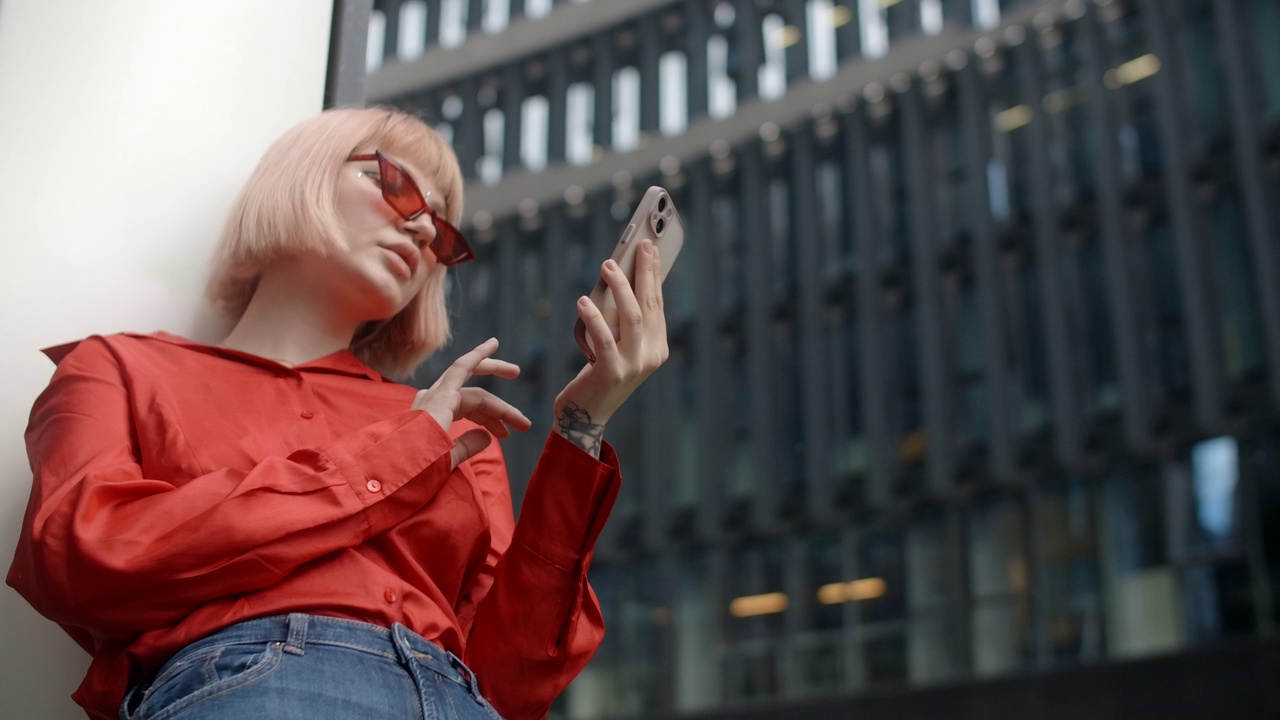 穿着红衣服的时髦金发女人在市中心打电话视频下载