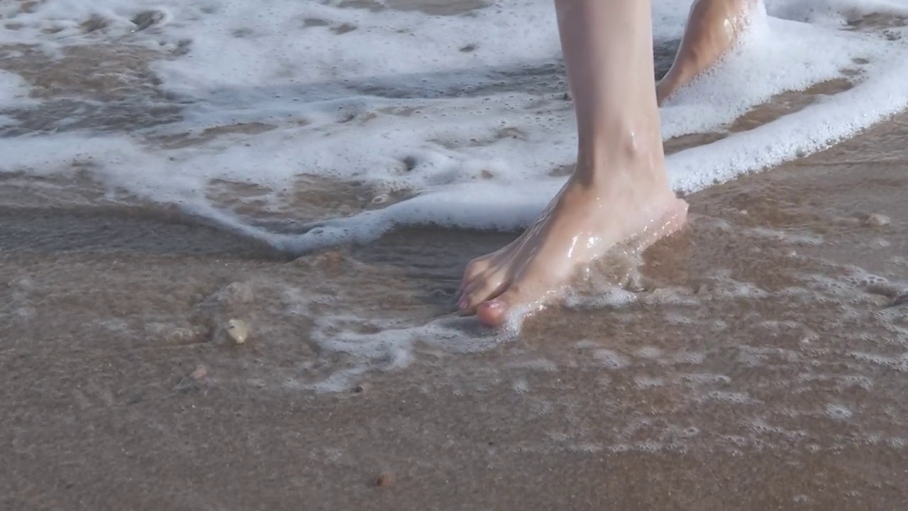 一个女人的脚在海边沙滩上的特写。视频素材