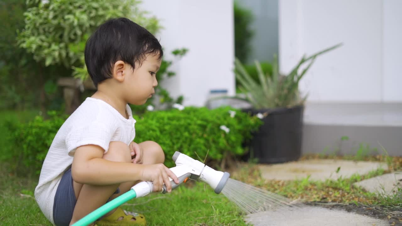 快乐的小男孩在花园里给植物和草坪洒水。视频素材