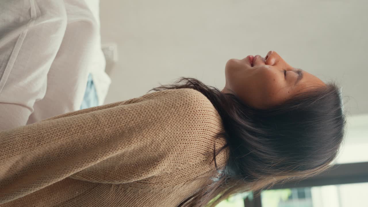 特写亚洲女孩，穿着白色的奶油睡衣，头朝下躺在枕头上，闭上眼睛，开心地微笑，在卧室里柔软的床上感到舒适，节日的早晨，窗外的阳光。女性早晨的感觉。视频素材