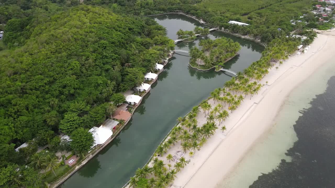 天空多云的海滩后面的绿色景观中的运河鸟瞰图视频素材