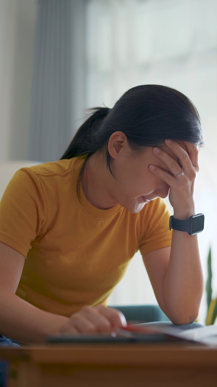 亚洲女性坐在沙发上，担心银行票据、抵押贷款债务和生活成本的账单支付问题。视频素材