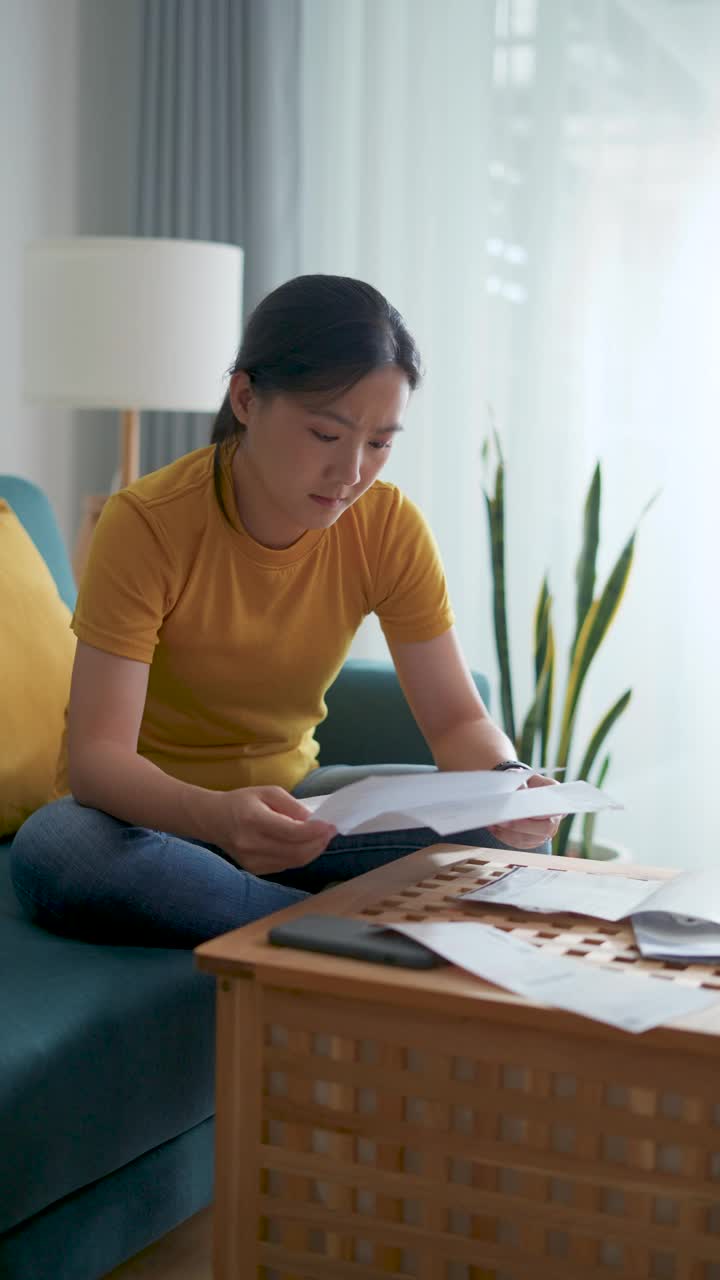 亚洲女性坐在沙发上，担心银行票据、抵押贷款债务和生活成本的账单支付问题。视频素材