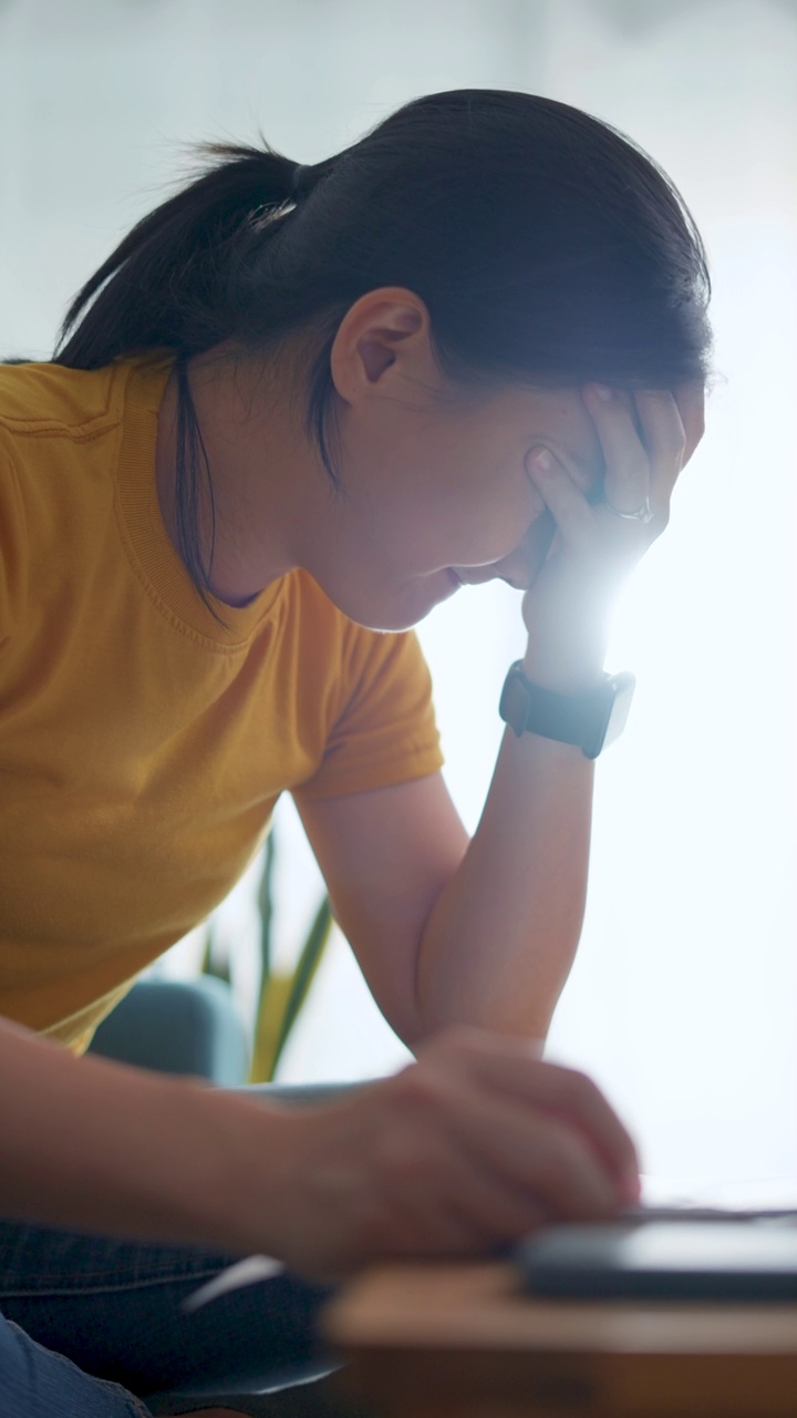 亚洲女性坐在沙发上，担心银行票据、抵押贷款债务和生活成本的账单支付问题。视频素材