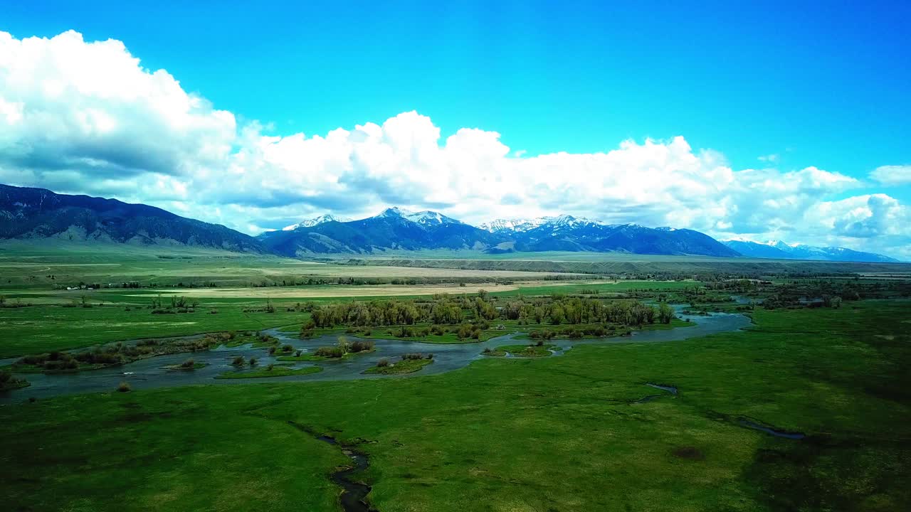 在多云的天空下，无人机在自然景观上空飞行，从空中锁定山脉附近的河流。蒙大拿比林斯视频素材