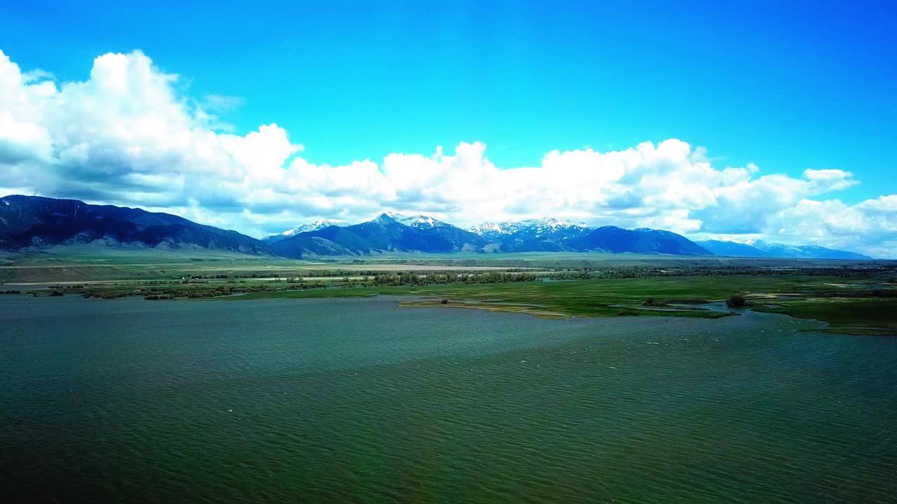 在多云的天空中，无人机在自然景观上向前飞行，在蒙大拿比林斯的山脉附近的河流航拍视频素材