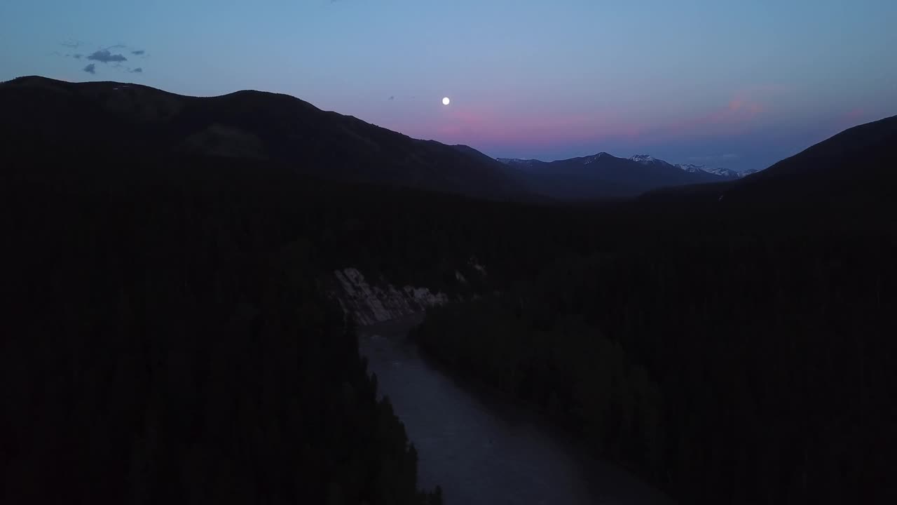 空中平移拍摄的河流剪影树木在山脉，无人机飞越自然景观对天空在黄昏-利比，蒙大拿州视频素材