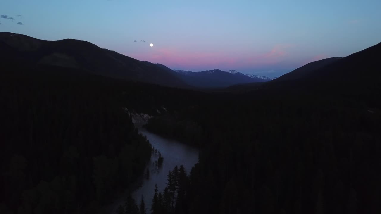 空中平移拍摄的河流在剪影山附近的树木，无人机飞越自然景观对天空在黄昏-利比，蒙大拿州视频素材