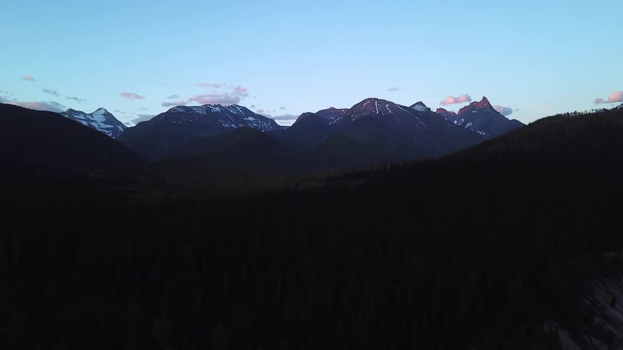 空中拍摄的河流在剪影山附近的树木中，无人机在黄昏时在自然景观上对着天空向后飞行-蒙大拿利比视频素材