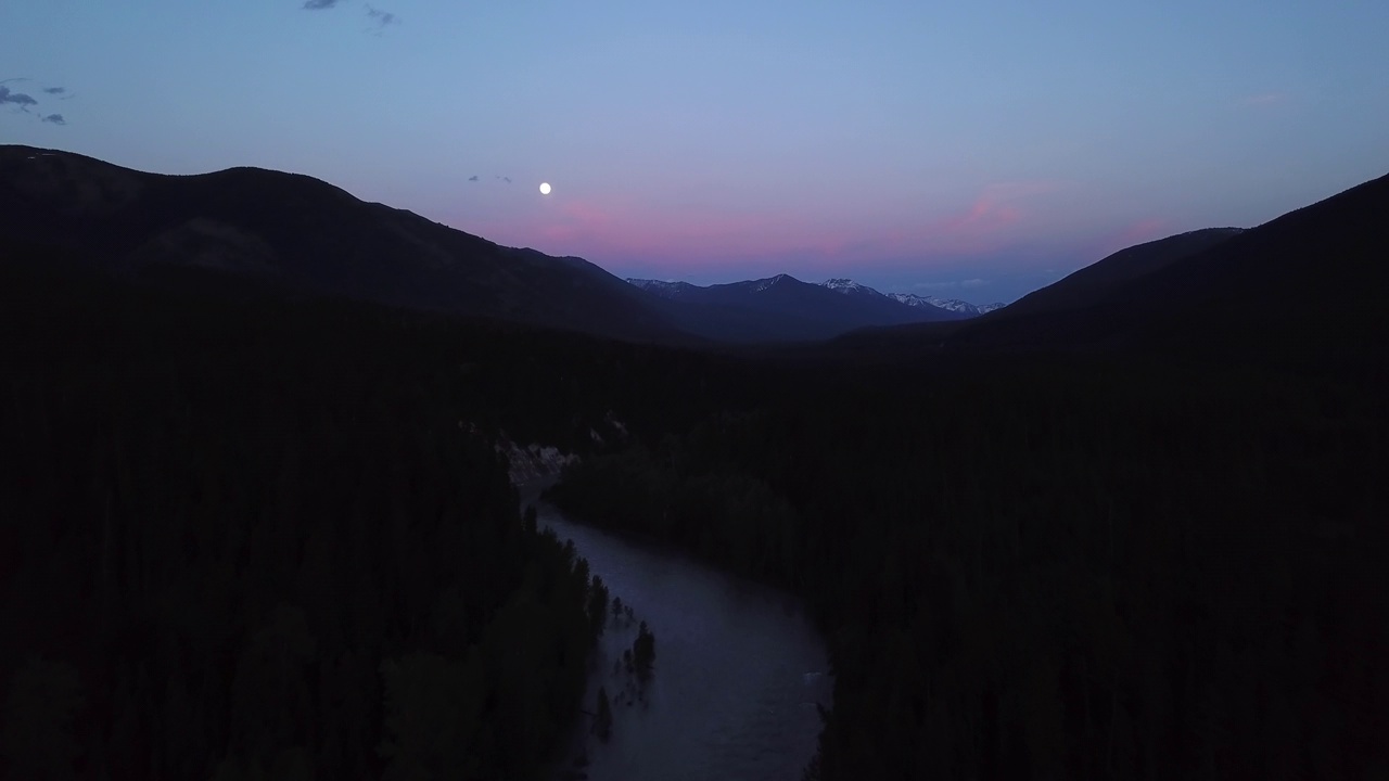 空中拍摄的河流在剪影山脉附近的树木中，无人机在黄昏时在自然景观上对着天空飞行-蒙大拿利比视频素材