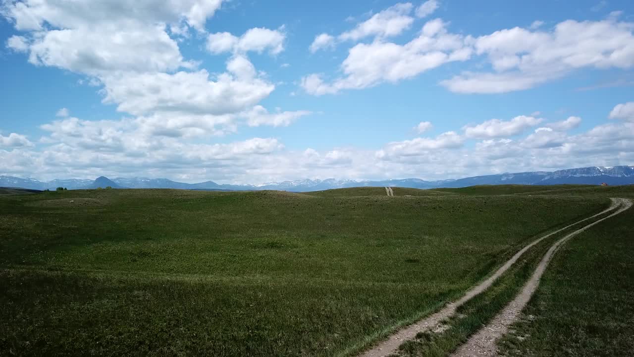 航拍:无人机向前飞行在绿色植物与土路在山附近的山对天空比林斯，蒙大拿州视频素材