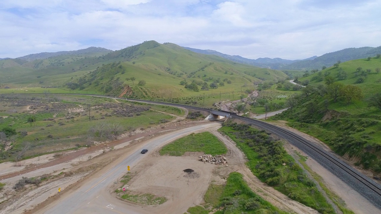 空中拍摄的汽车在铁路桥附近的道路上，无人机在绿色景观上向前飞行-贝克斯菲尔德，加利福尼亚州视频素材