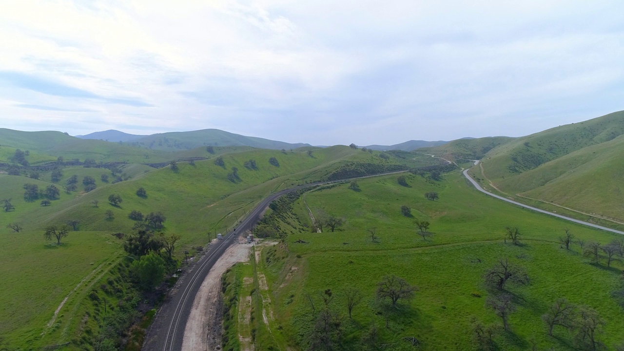 铁路和公路附近的植物和树木航拍，无人机在多云的天空下飞越自然绿色景观-贝克斯菲尔德，加利福尼亚州视频素材