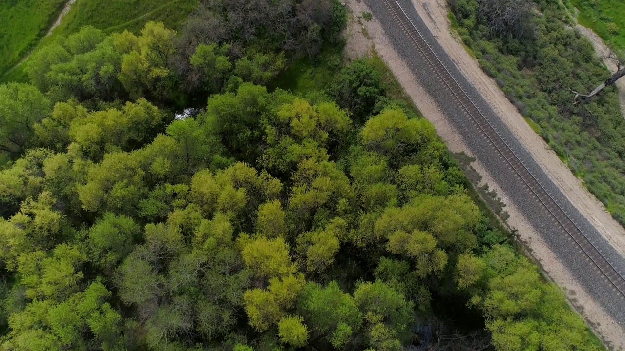 在绿色植物中的公路和铁路的空中倾斜镜头，无人机在多云的天空中飞过自然景观-贝克斯菲尔德，加利福尼亚州视频素材