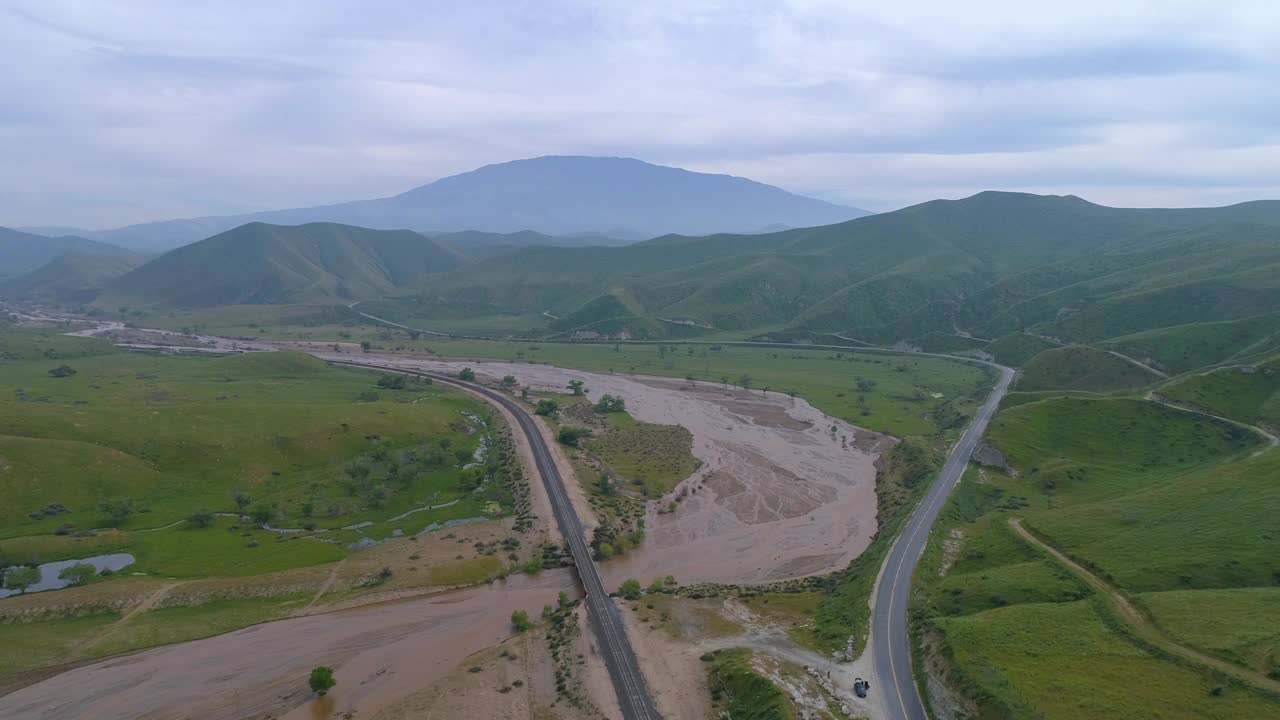 航拍的铁路桥上的河流附近的道路对着天空，无人机向前飞行在绿色景观对着天空-贝克斯菲尔德，加州视频素材