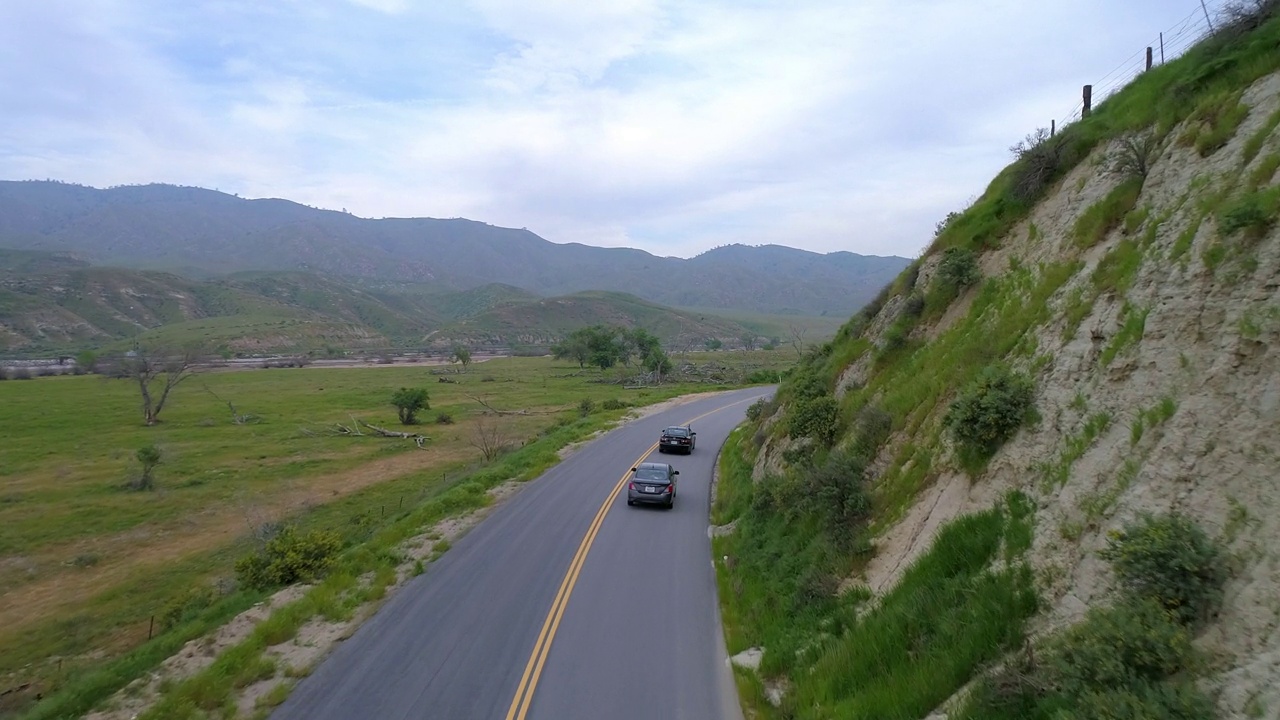 在多云的天空中，汽车在绿色植物附近的道路上飞行，无人机在景观上向前飞行——加利福尼亚州贝克斯菲尔德视频素材