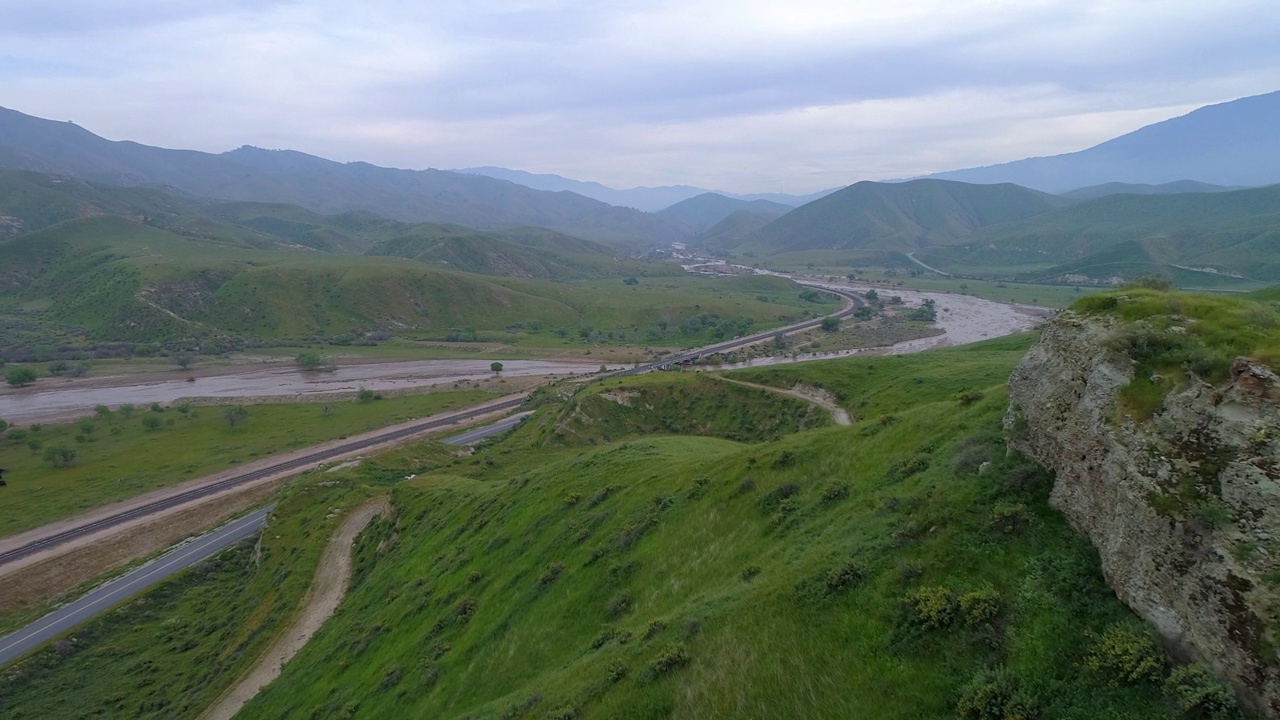 航拍的绿色山脉附近的河流对着天空，无人机下降向前在公路和铁路轨道-贝克斯菲尔德，加州视频素材